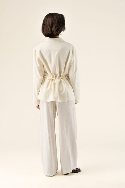 Person wearing a cream-colored outfit with wide-leg pants on a beige background