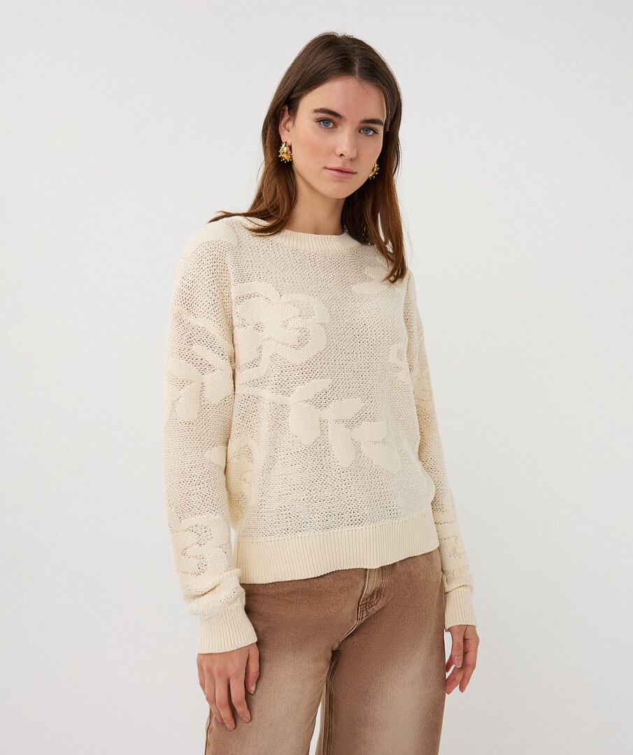 Woman wearing a cream sweater with a subtle pattern on a white background
