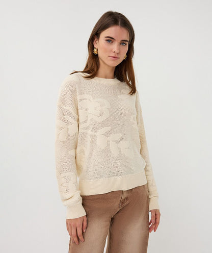 Woman wearing a cream sweater with a subtle pattern on a white background