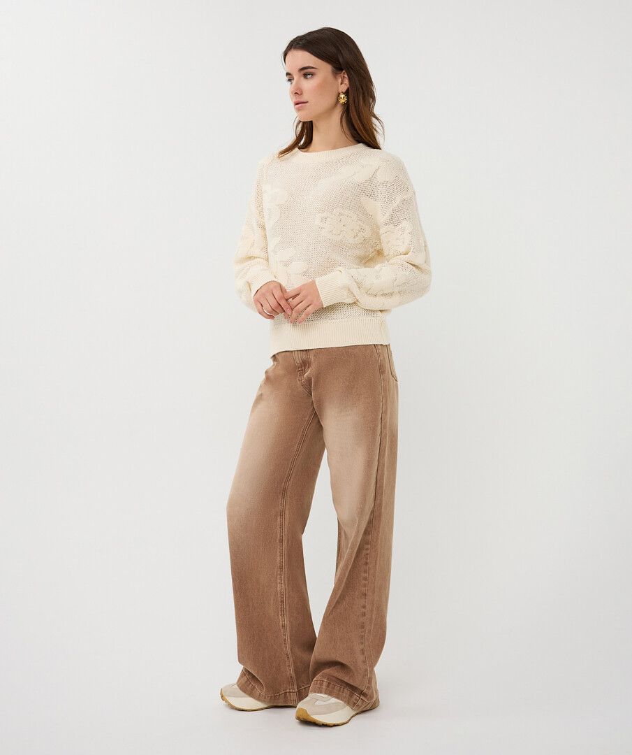Woman wearing a cream sweater and brown pants on a white background