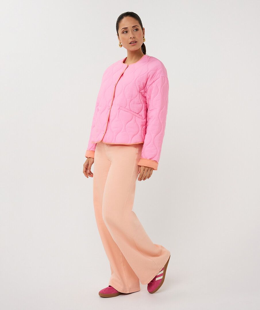 Woman wearing a pink quilted jacket and peach pants on a white background