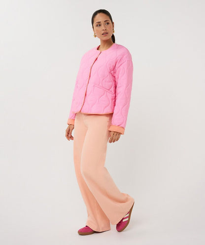Woman wearing a pink quilted jacket and peach pants on a white background