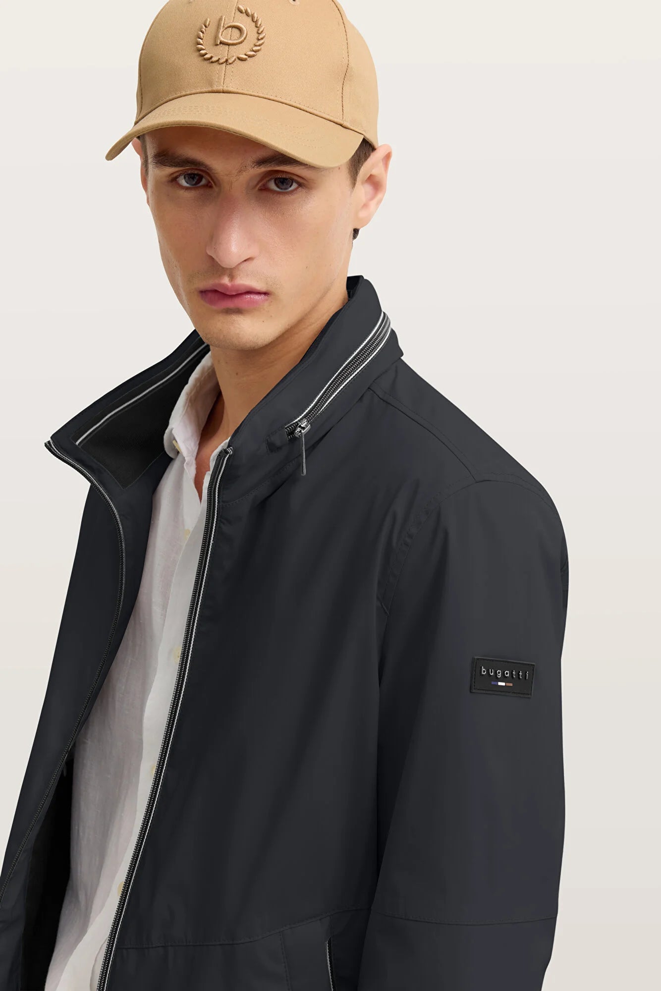 Man wearing a black jacket and beige cap on a light background