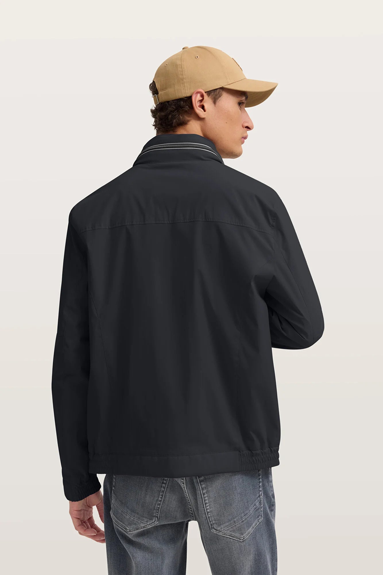 Person wearing a black jacket and beige cap on a plain background