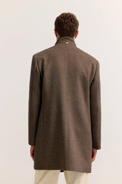 A man viewed from behind wearing a brown wool-blend coat with a high stand collar and light beige trousers, set against a plain off-white studio background.
