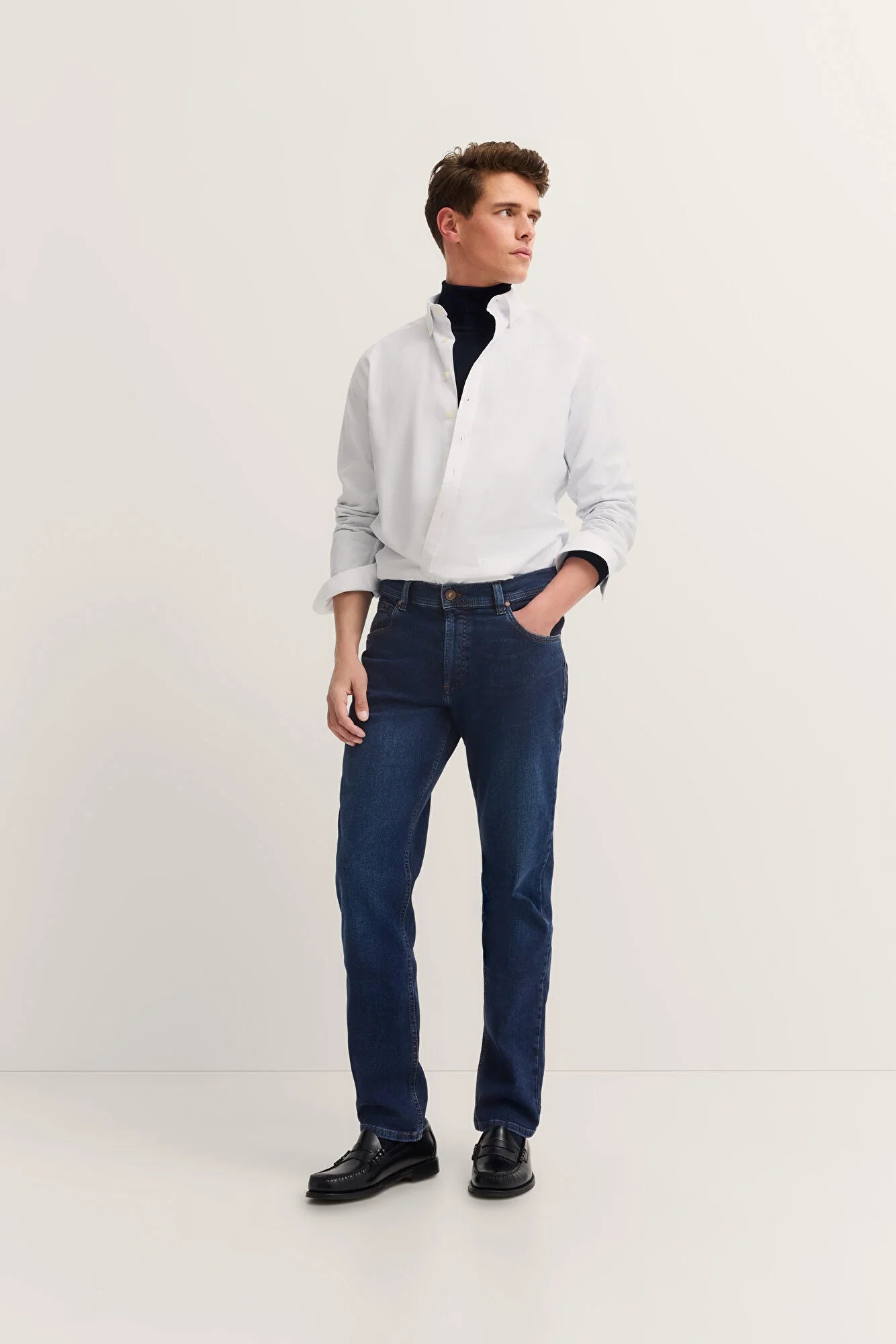 Man wearing a white shirt, dark blue jeans, and black shoes on a white background
