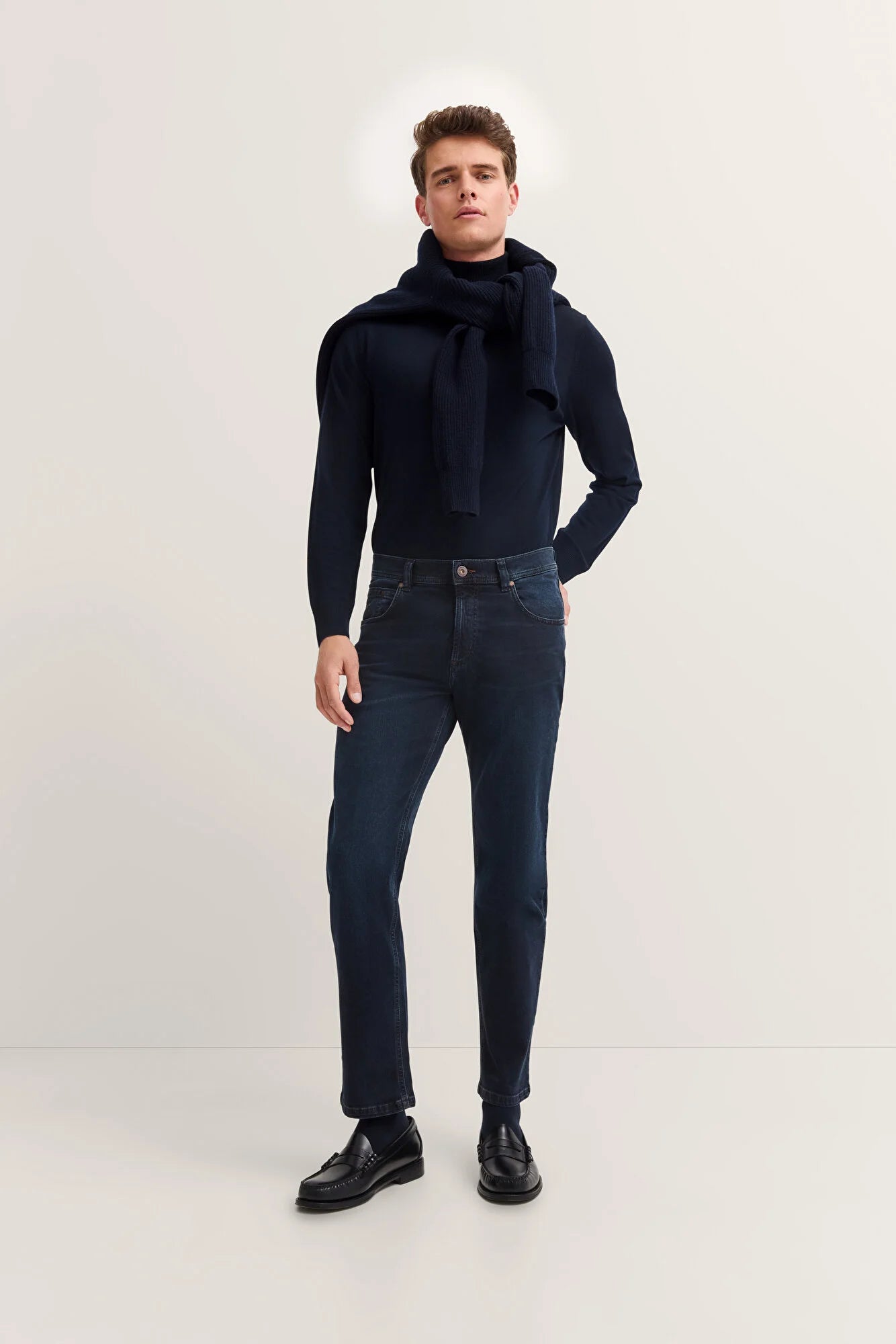 Man wearing a navy sweater and jeans on a white background