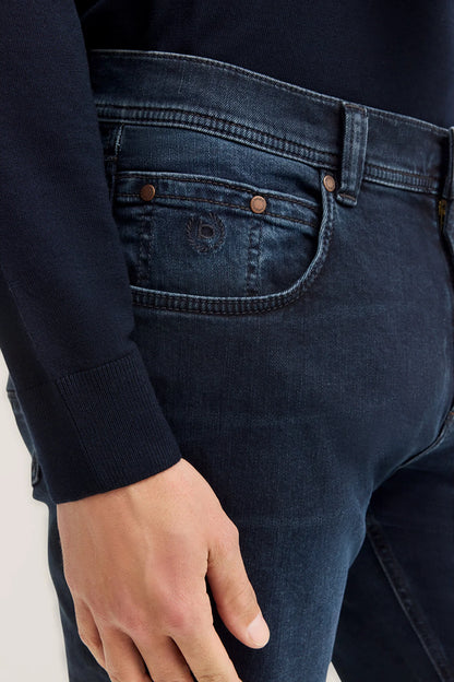 Close-up of a person wearing dark blue jeans with a plain background