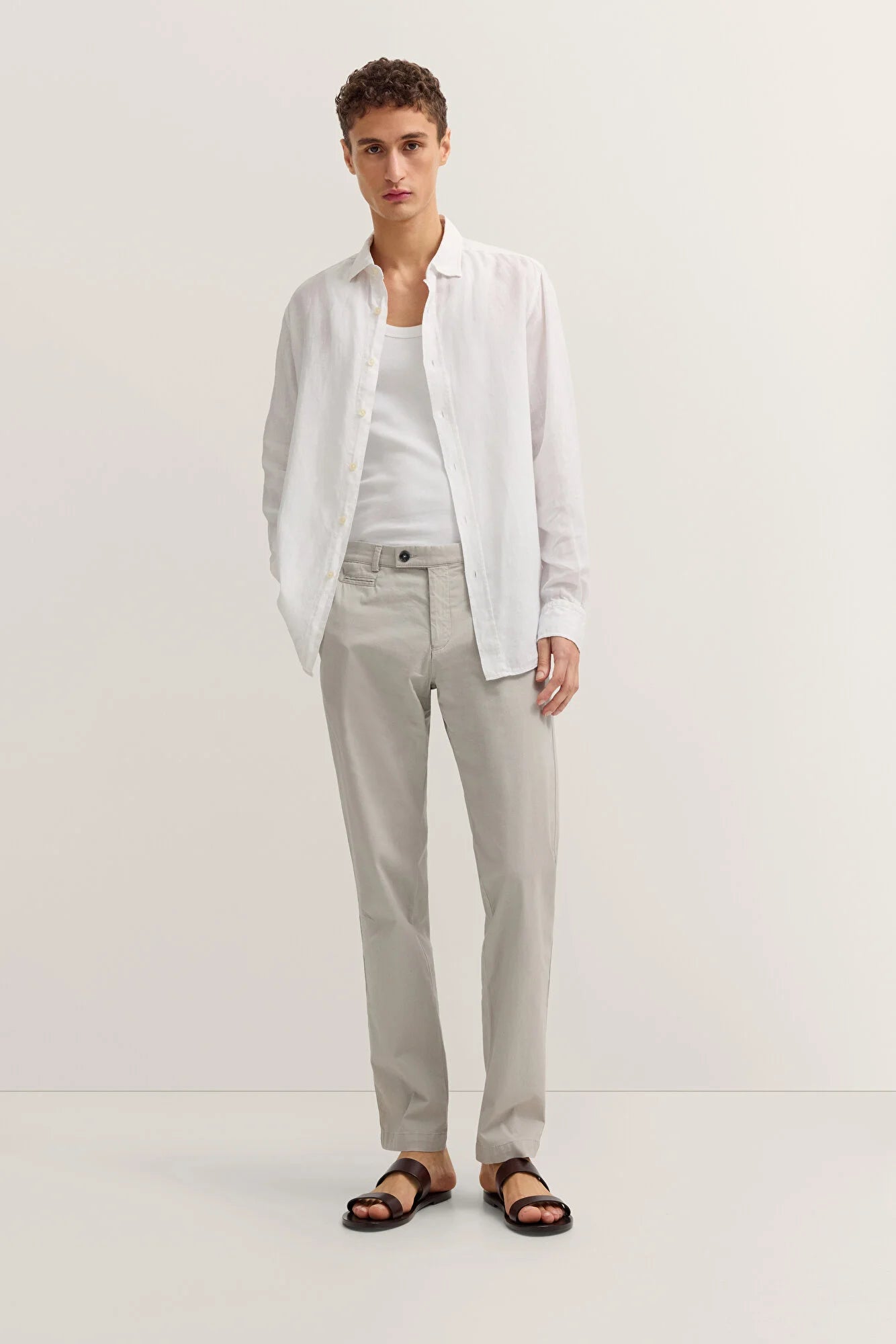 Man wearing a white shirt, light gray pants, and sandals on a white background