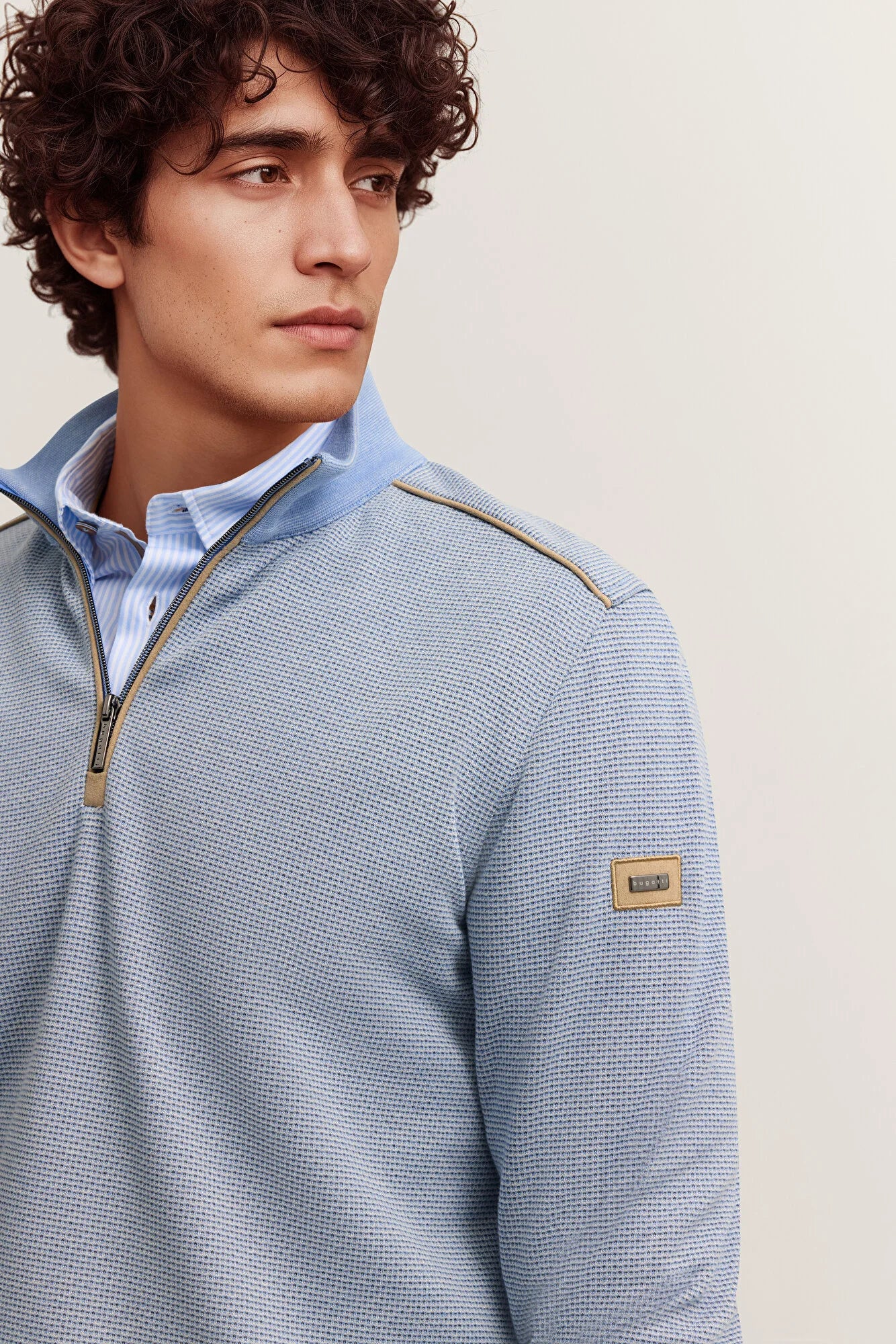 Man wearing a blue textured sweater with a beige label against a light background