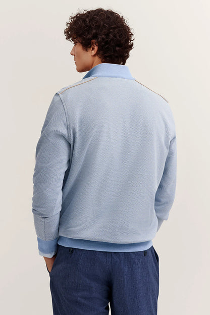 Person wearing a light blue sweater with a white collar against a plain background