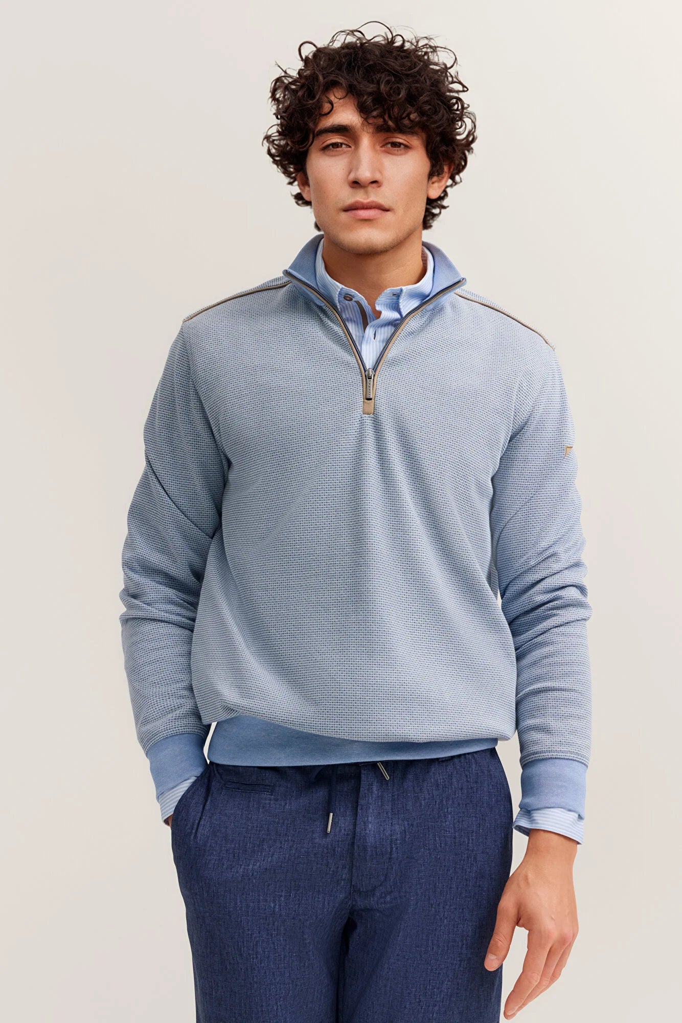 Man wearing a light blue pullover with a zipper on a plain background