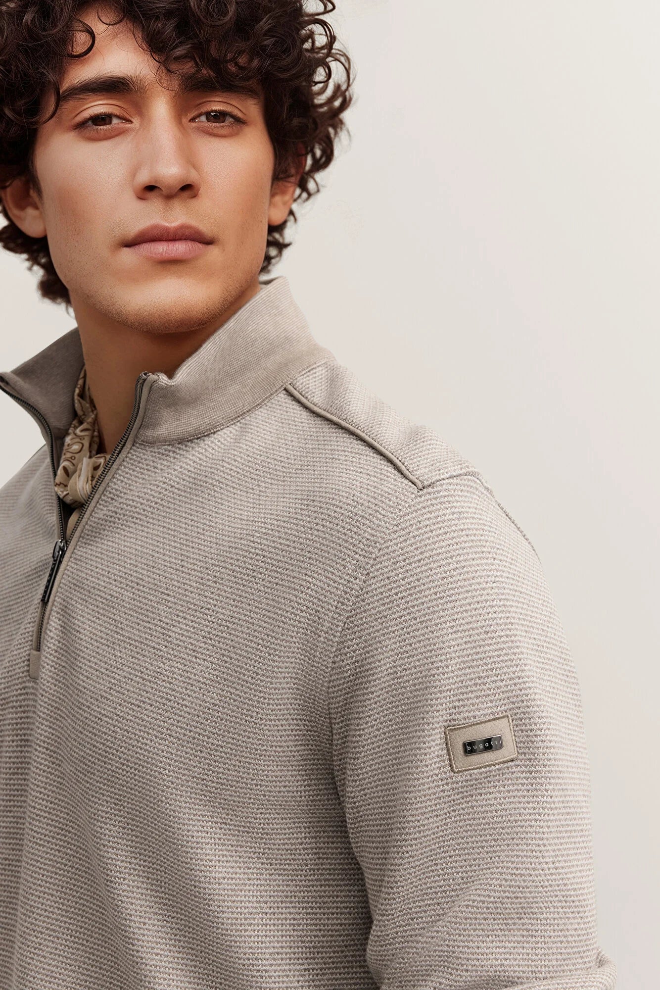 Man wearing a textured gray sweater with a brand logo on a light background