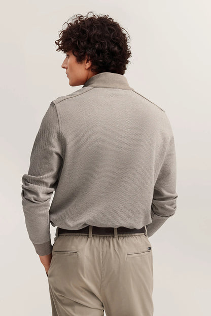 Man wearing a gray sweater and beige pants against a plain background