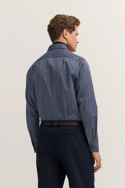Man wearing a patterned blue shirt and dark pants on a light background